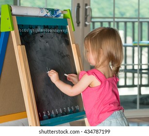 Young Two Year Old Girl Drawing With Chalk On Blackboard And Using Both Hands Ambidextrously