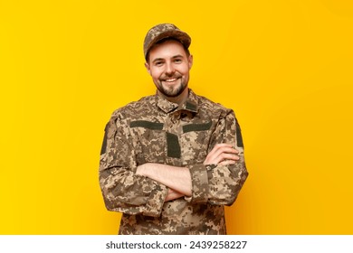 young Ukrainian army soldier in pixel camouflage uniform stands with his arms crossed on a yellow isolated background, Ukrainian military cadet looks at the camera and smiles - Powered by Shutterstock