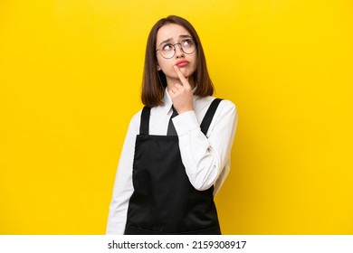 Young Ukrainian Waitress Woman Isolated On Yellow Background Having Doubts