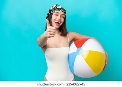 Young Ukrainian woman holding beach ball isolated on blue background with thumbs up because something good has happened