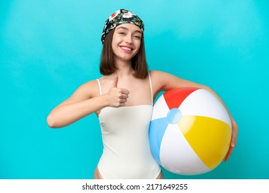 Young Ukrainian woman holding beach ball isolated on blue background giving a thumbs up gesture