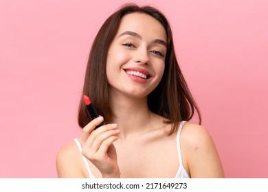 Young Ukrainian woman isolated on pink background holding red lipstick