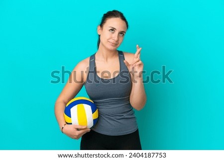 Young Ukrainian woman playing volleyball isolated on blue background with fingers crossing and wishing the best