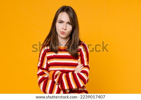 Young unhappy dissatisfied offended sad caucasian woman in red striped sweatshirt hold hands crossed folded look camera isolated on plain yellow background studio portrait. People lifestyle concept