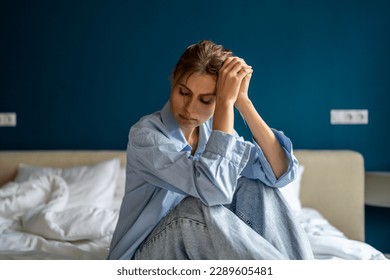 Young unhappy woman sitting on bed at home, waking up depressed, suffering from depression, feeling sad and miserable. Female suffering from post-traumatic stress disorder. Women and mental health - Powered by Shutterstock