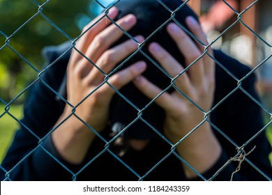 Young Unidentifiable Teenage Boy  Holding Hes Head At The Correctional Institute ,conceptual Image Of Juvenile Delinquency, Focus On The Wired Fence.