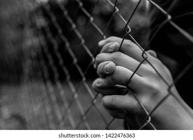 Young Unidentifiable Teenage Boy Holding The Wired Garden  Praying At The Correctional Institute In Black And White, Conceptual Image Of Juvenile Delinquency, Focus On The Boys Hand.