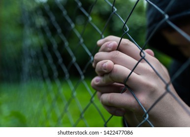 Young Unidentifiable Teenage Boy Holding The Wired Garden  Praying At The Correctional Institute , Conceptual Image Of Juvenile Delinquency, Focus On The Boys Hand.