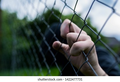 Young Unidentifiable Teenage Boy Holding The Wired Garden At The Correctional Institute, Conceptual Image Of Juvenile Delinquency, Focus On The Boys Hand.