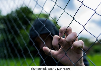 Young Unidentifiable Teenage Boy Holding The Wired Garden At The Correctional Institute, Conceptual Image Of Juvenile Delinquency, Focus On The Boys Hand.