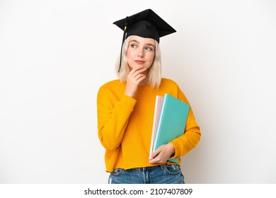 Young university caucasian woman graduate isolated on white background looking up while smiling