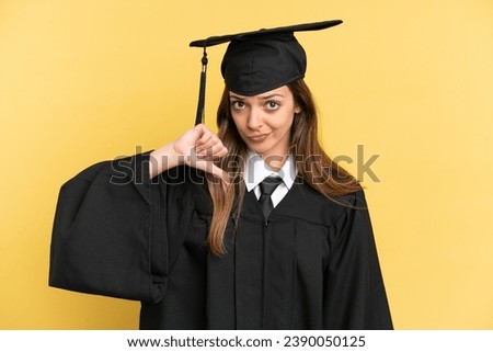 Young university graduate isolated on yellow background showing thumb down with negative expression