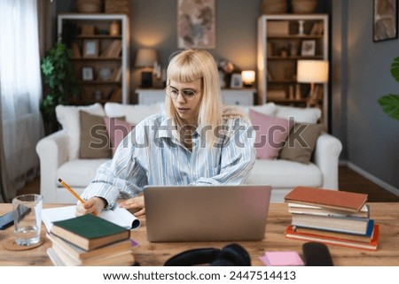 Young university student, college woman or girl, study for final exam at home. Young female learning and educate herself using books and laptop computer for e-learning. Knowledge is power concept.