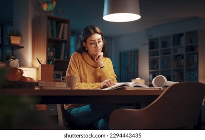 Young university student reading books late at night, she is studying and preparing for her exams - Powered by Shutterstock