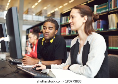 Young University Students Sitting At Table Using Computers For Research. Young People Taking Information From Computer For Their Study In Modern Library.