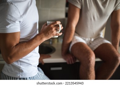 Young unrecognizable  interracial gay couple in pajamas having tea in a kitchen. Handsome homosexual men, Caucasian and Mixed race, sitting on counter, enjoy morning at home. LGBT family  concept.  - Powered by Shutterstock