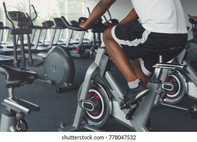 Young Unrecognizable Man On Exercise Bike In Gym. Male Legs In Fitness Club. Healthy Lifestyle Concept