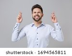 Young unshaven business man in light shirt posing isolated on grey background. Achievement career wealth business concept. Waiting for special moment keeping fingers crossed, eyes closed, making wish