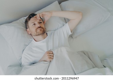 Young Upset And Tired Bearded Man Lying On Bed With Open Eyes And Cannot Sleep, Male Having Insomnia Problem Or Sleeping Troubles. Bedtime And Rest Difficulty Concept