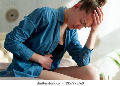 Young upset unhappy woman suffering from menstruation pain, PMS at home. Abdomen and stomach pain during criticals days. Health problems