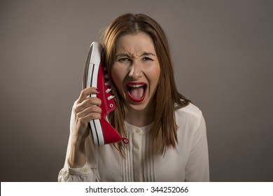 Young upset woman using a red shoe like a telephone holding it near her face and talking