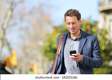 Young urban businessman professional on smartphone walking in street using app texting sms message on smartphone wearing jacket on Passeig de Gracia, Barcelona, Catalonia, Spain.