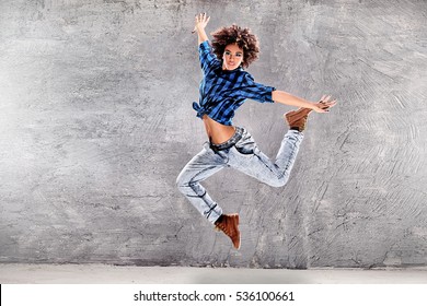 Young urban hip hop dancer jumping and dancing with grunge concrete wall background. Girl with afro hair.