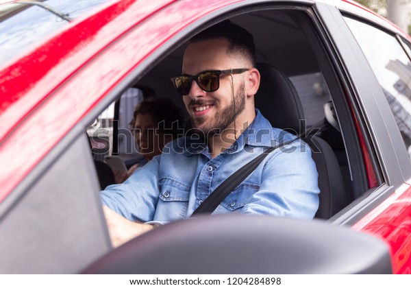 Young urban professional\
driver wearing denim shirt taking passenger to ride in private\
vehicle transportation. Concept of commute, transport service,\
mobility.