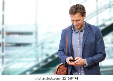 Young urban professional man using smart phone in office building indoors. Businessman holding mobile smartphone using app texting sms message wearing suit jacket and bag.