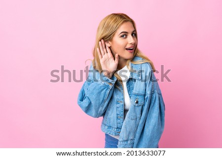 Young Uruguayan blonde woman over isolated pink background listening to something by putting hand on the ear
