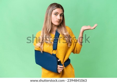 Young Uruguayan woman with broken arm and wearing a sling over isolated background having doubts while raising hands