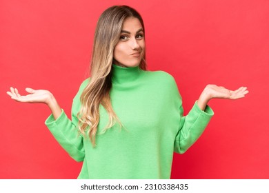 Young Uruguayan woman isolated on red background having doubts while raising hands - Shutterstock ID 2310338435