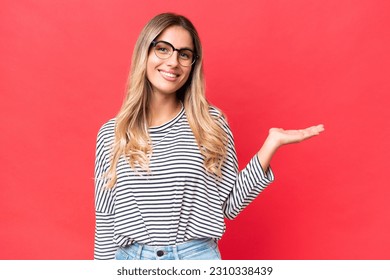 Young Uruguayan woman isolated on red background holding copyspace imaginary on the palm to insert an ad