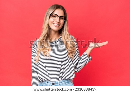 Young Uruguayan woman isolated on red background holding copyspace imaginary on the palm to insert an ad