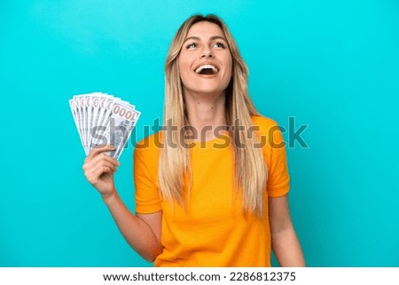 Young Uruguayan woman taking a lot of money isolated on blue background laughing