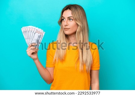 Young Uruguayan woman taking a lot of money isolated on blue background looking to the side