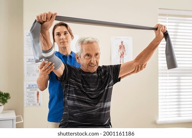 Young v working with senior patient in rehabilitation center. Trainer assisting senior patient in exercising with resistance band in private clinic. Rehabilitation physiotherapy worker working. - Powered by Shutterstock