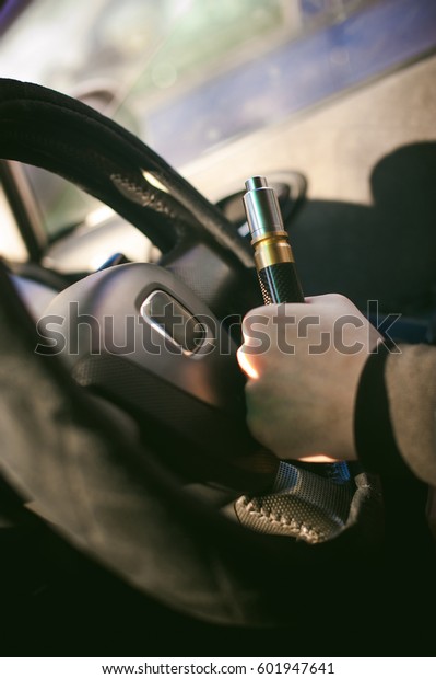 young vaper man\
with beard vaping mechanical mod. Guy smokes an electronic\
cigarette by blowing a smoke vapor. Holds in hand Sitting at the\
wheel of a car \
background