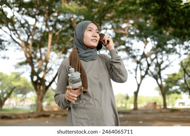 Young veiled asian muslim woman wiping face with towel in the park while holding a bottle of drink. Outdoor sport concept - Powered by Shutterstock