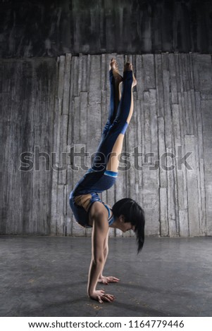 Young very flexible female acrobat standing on hand over gray background in photo studio