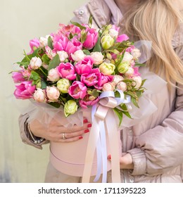 Young Very nice florist woman holding a beautiful colourful blossoming flowers bouquet of fresh pink tulips and Alstroemeria in big pink hat box. Copy space. 
