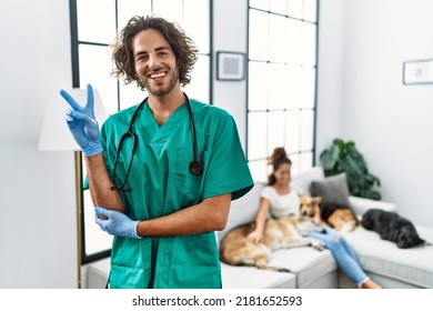 Young veterinarian man checking dogs at home smiling with happy face winking at the camera doing victory sign. number two. 