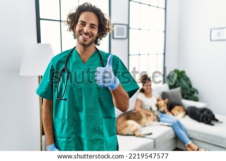 Young veterinarian man checking dogs at home smiling happy and positive, thumb up doing excellent and approval sign 