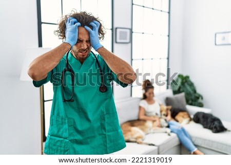 Young veterinarian man checking dogs at home suffering from headache desperate and stressed because pain and migraine. hands on head. 
