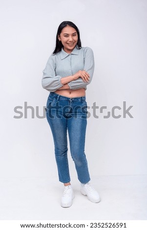 An young vibrant asian woman with mid-length hair in a long sleeved cutoff blouse and blue jeans. Possible college student. Isolated on a white backdrop.