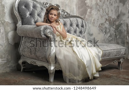 Young Victorian princess sitting on a silver sofa in a white dress