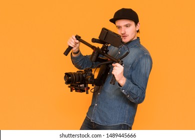 A young videographer using stabilization for a camera. The operator demonstrates his skill and shoots video on the dslr camera on an orange background. Creating a video concept