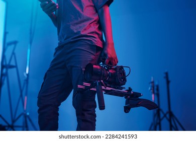 Young videomaker using smartphone while standing with professional camera to make content