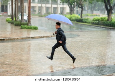 Young Vietnamese Businessman Wearing Classical Suit Crossing Road While Hurrying Home After Hard Working Day In Pouring Rain, He Holding Umbrella In Hand