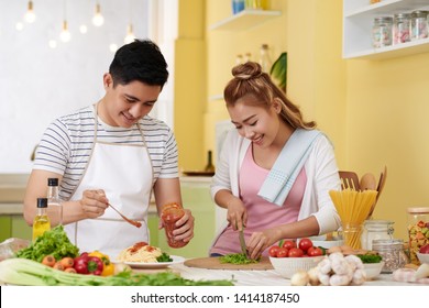 Young Vietnamese couple cooking spaghetti and salad for dinner togther